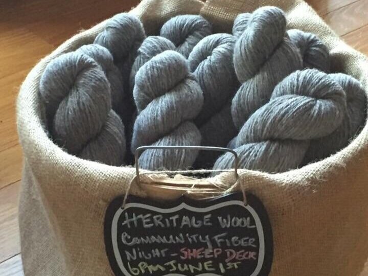 A burlap basket filled with gray Heritage wool skeins, promoting a Community Fiber Night event on June 1st at 6 PM on Sheep Deck.